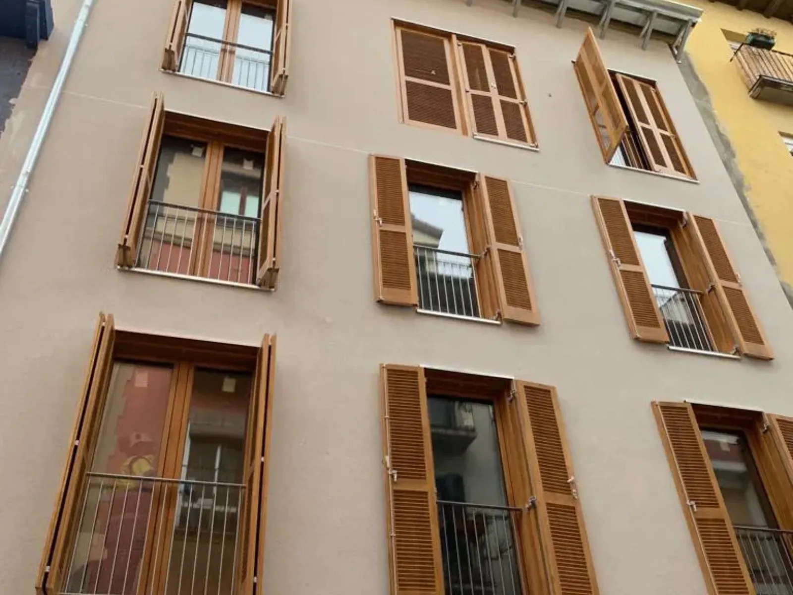 Fachada de edificio con ventanas de madera y contraventanas abiertas